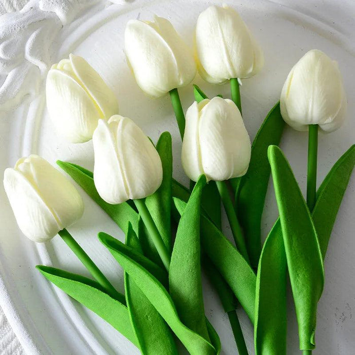 Artificial white tulips with green leaves on a decorative white plate.