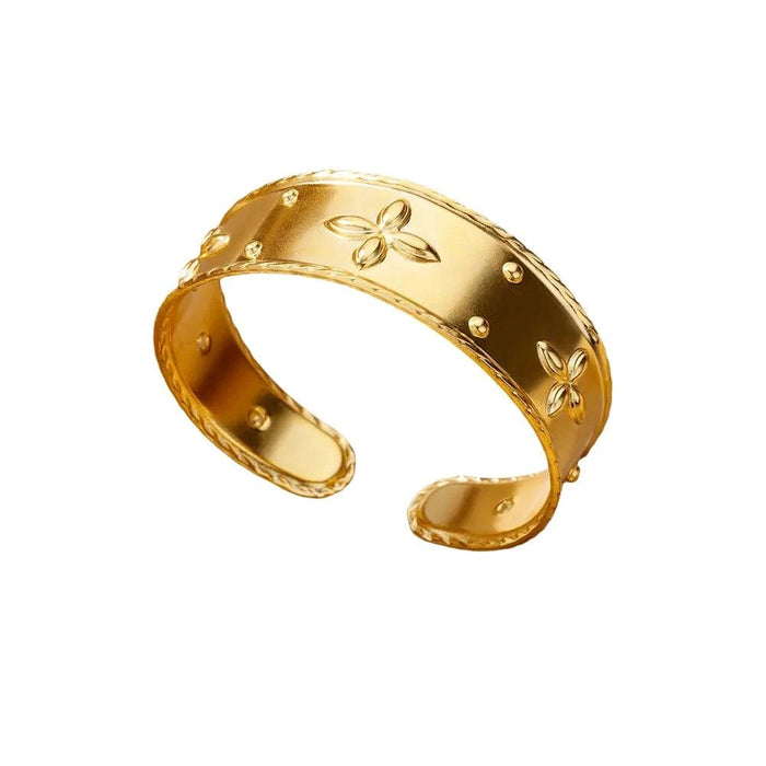 Wide gold cuff bracelet with floral engravings and raised dots, displayed on a white background.