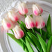 A bunch of artificial cream tulips with pink tips on a white plate.