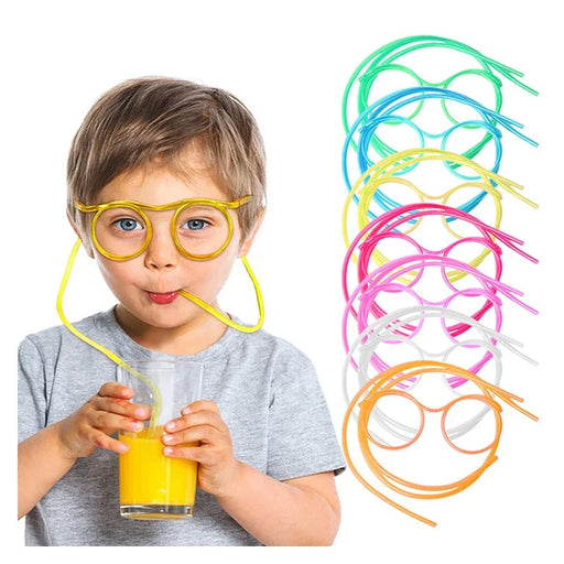 A young boy wearing yellow drinking straw glasses while drinking orange juice from a glass. Several other colors of the straw glasses are shown on the side, including green, blue, pink, and white.