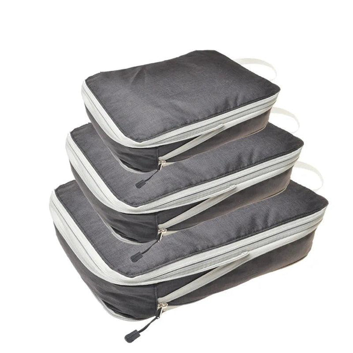 Three dark gray packing cubes with gray zippers and handles, stacked on top of each other. Each cube has a zipper pull with a black tab.