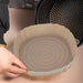 A close-up image of a person's hand holding a beige silicone air fryer liner with a spiral design at the bottom, placed next to an open air fryer basket.