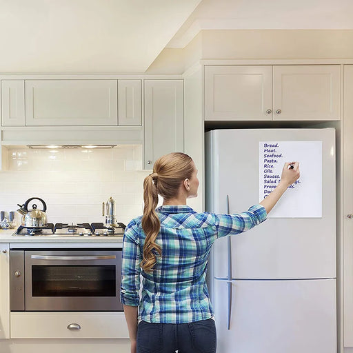 A woman writing on a whiteboard mounted on her refrigerator in a modern kitchen.