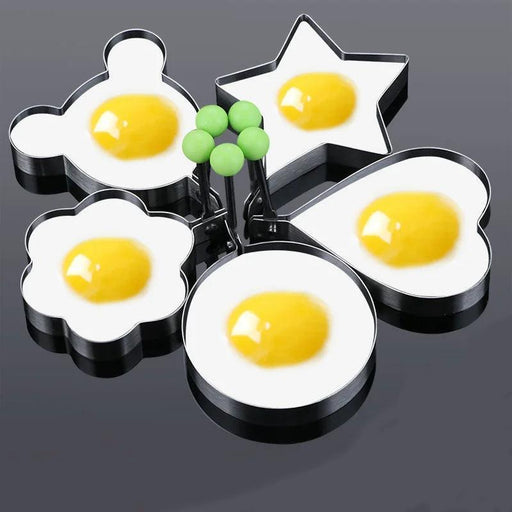 Five fried eggs cooked in metal egg molds of different shapes (bear, star, heart, flower, and circle) on a dark surface. The yolks are centered and intact in each egg, showing the molds' shapes clearly.