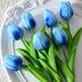 A bunch of artificial tulips with cream and orange petals and green leaves on a white plate.