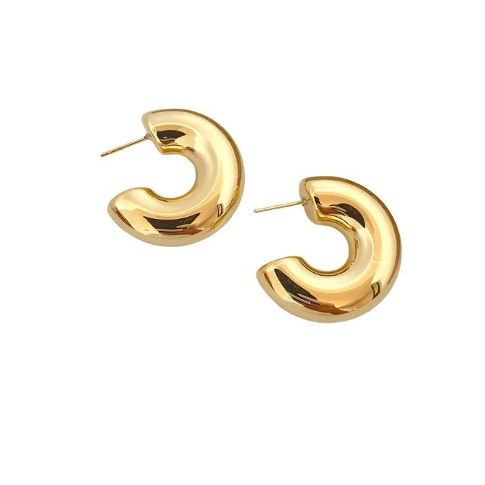 A pair of chunky, gold hoop earrings. These earrings have a similar smooth and polished finish but with a slightly more open and curved shape.