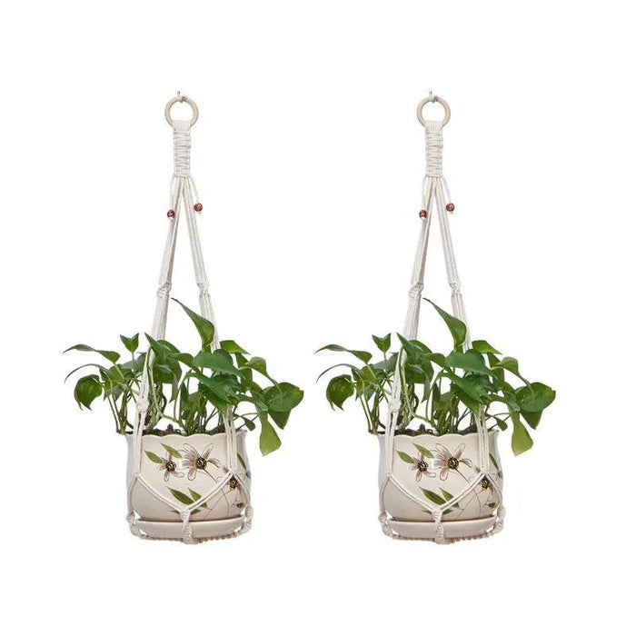 Two identical hanging macrame plant holders, each holding a green plant in a white pot with floral designs. The holders have wooden rings for hanging and are decorated with small wooden beads.