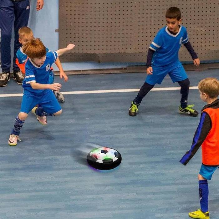 Several young boys playing with a hover soccer ball in an indoor sports setting.