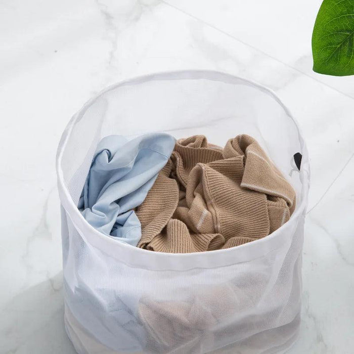 Open white mesh laundry bag filled with a light blue shirt and a beige knitted sweater, placed on a marble surface. The bag is designed for washing delicate clothing, offering protection while maintaining cleaning efficiency.