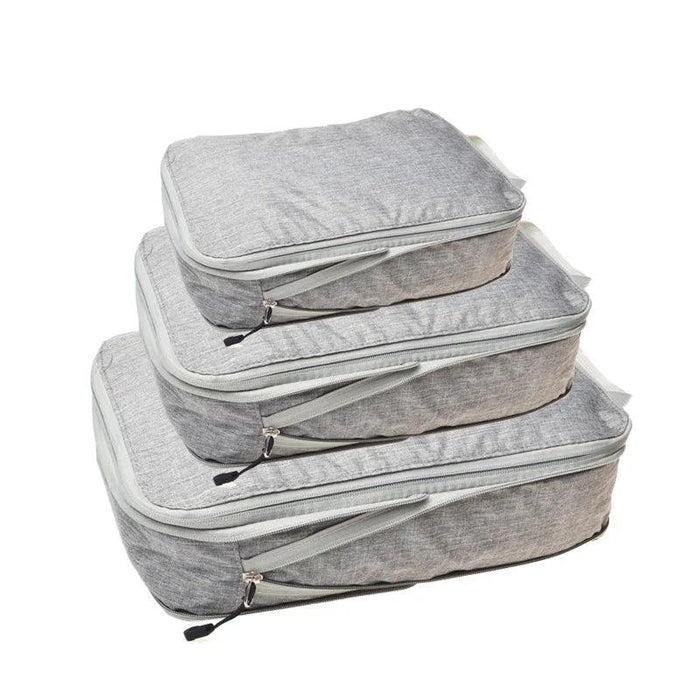 Three light gray packing cubes with gray zippers and handles, stacked on top of each other. Each cube has a zipper pull with a black tab.