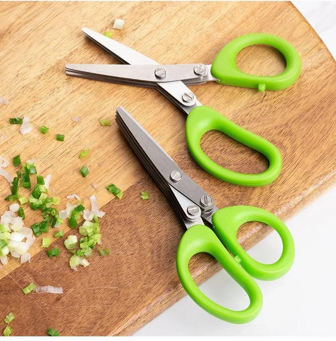 Green-handled herb scissors on a wooden cutting board with chopped green onions.