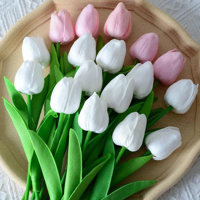 A collection of artificial tulips, mostly white with a few light pink ones, arranged on a beige plate with green leaves.