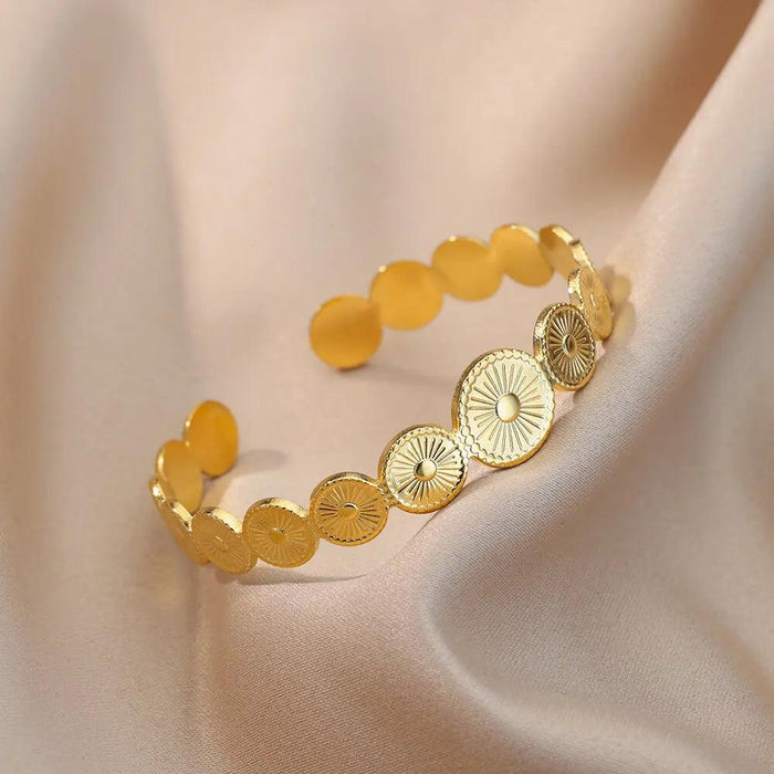 Gold bracelet with circular sunburst designs on a beige satin fabric.