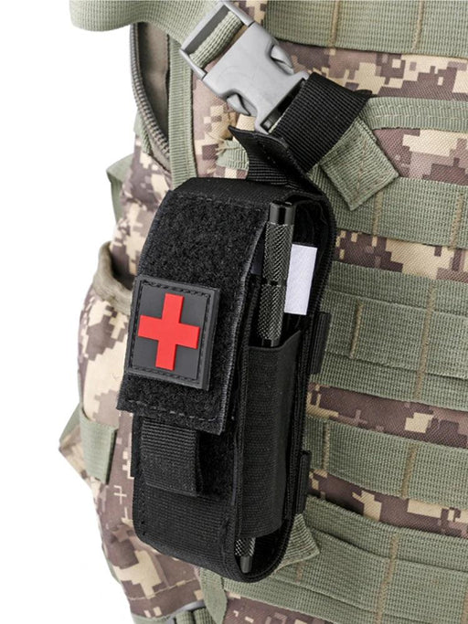 A black medical pouch with a red cross attached to a camouflage tactical vest, showing the tourniquet inside.