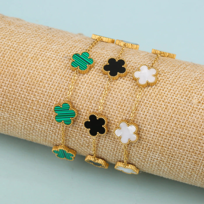 A set of gold bracelets featuring flower-shaped pendants in green, black, and white, each with a unique design, displayed on a burlap roll.