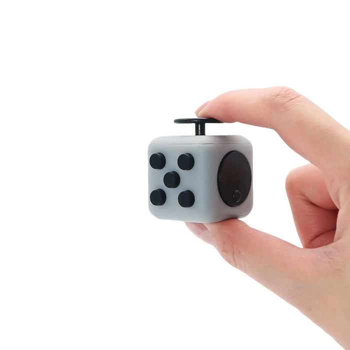 A person holding a small grey and black fidget cube with various buttons and dials.