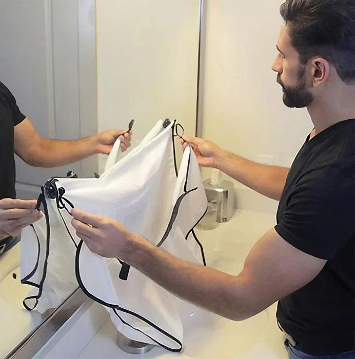 A man setting up a white beard trimming bib in front of a mirror.