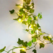 A close-up view of a string of green ivy adorned with bright lights against a plain background. This simple yet beautiful decoration is versatile, suitable for enhancing both indoor and outdoor spaces with a touch of natural elegance and soft lighting.